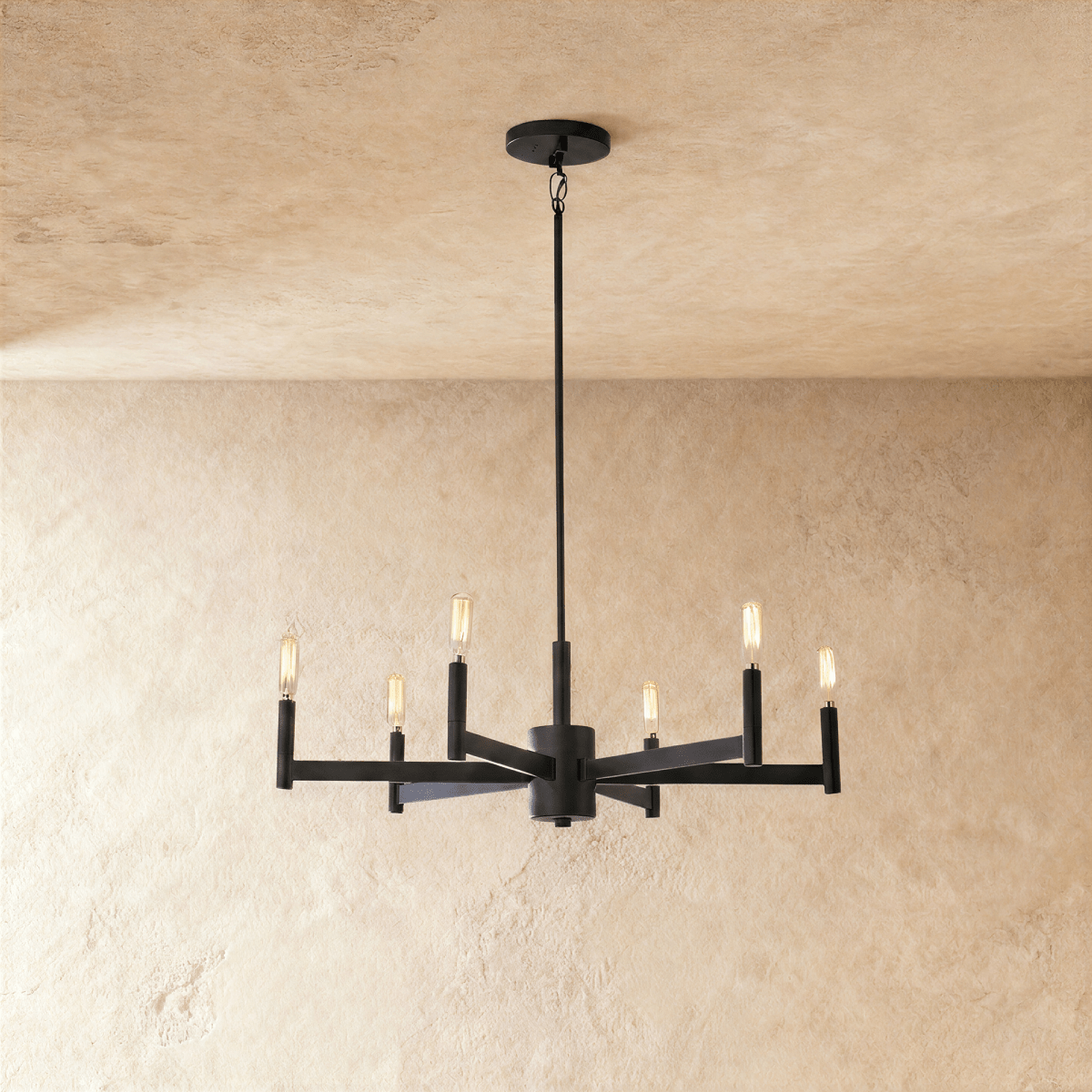 Clérachic six-arm chandelier in matte black with filament-style bulbs on slim candle tubes, hung from a rod against limewash.