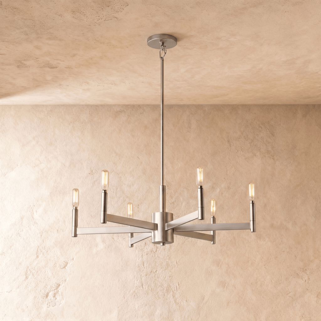Clérachic six-arm chandelier in champagne gold with filament bulbs on square-section arms, hung from a rod on a limewash wall.
