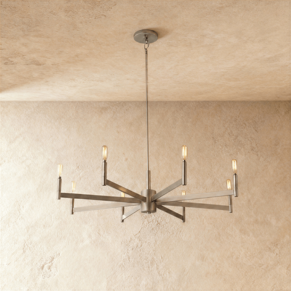 Clérachic eight-arm chandelier in champagne gold with filament bulbs on straight bars, centred on a limewash wall.