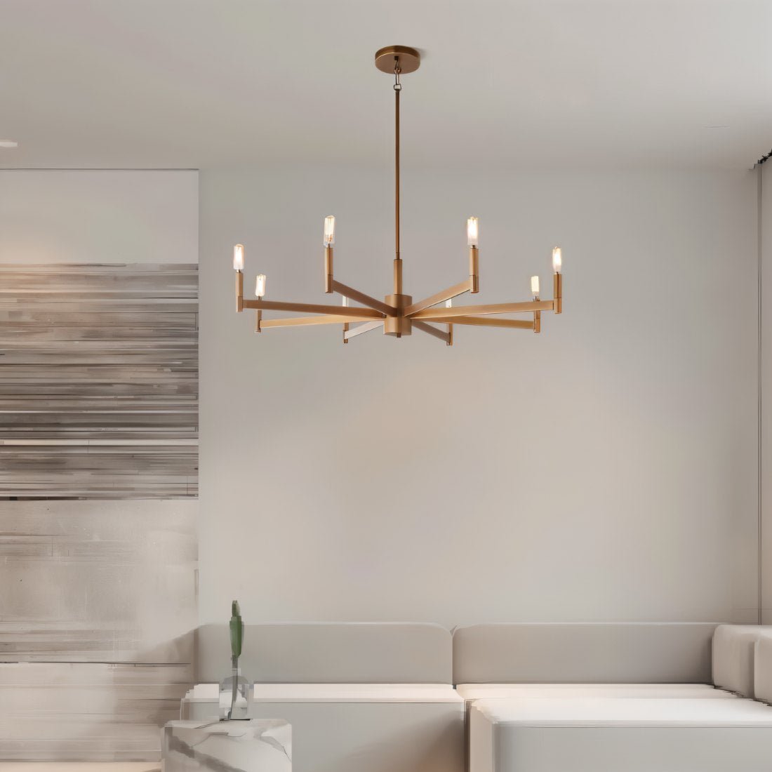 Clérachic eight-arm gold chandelier above a pale sofa in a calm living room with a brushed abstract panel at the left.