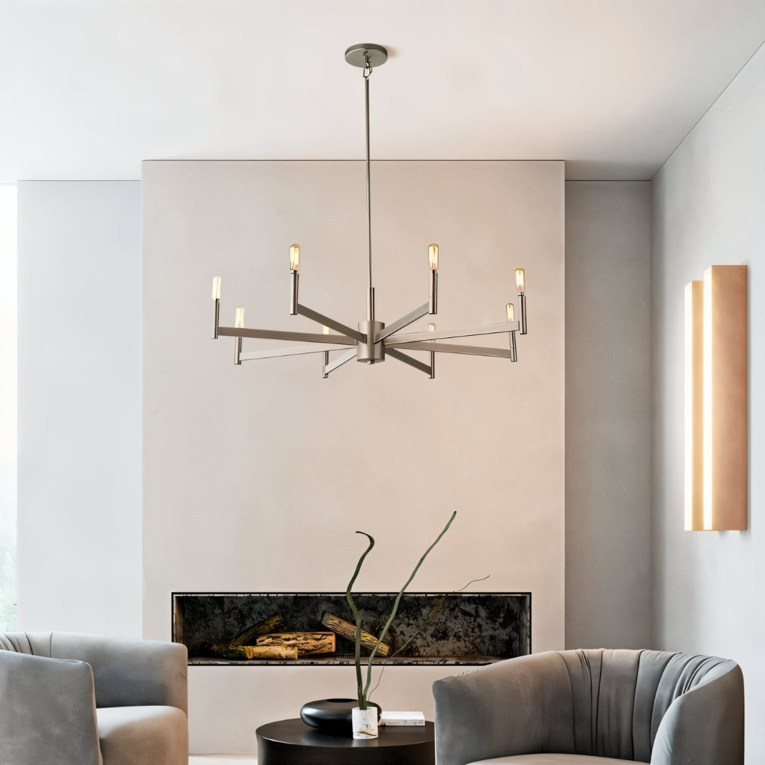 Clérachic eight-arm chandelier in champagne gold above grey armchairs, a low fireplace niche and a black round coffee table.