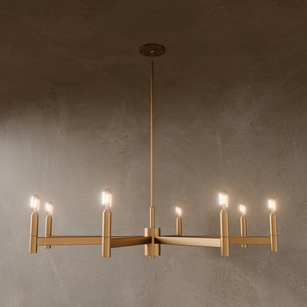 Clérachic wide eight-arm chandelier in satin gold with lit filament bulbs on straight bars, against a dark plaster wall.