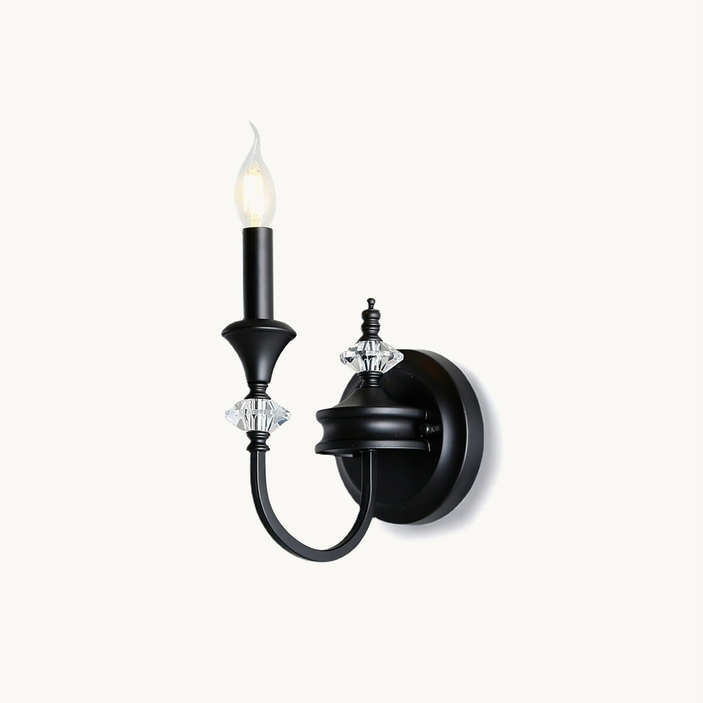 Single-arm Clérachic wall light in black on a plain white backdrop, a candle-style bulb above crystal accents on a curved iron arm.