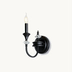 Single-arm Clérachic wall light in black on a plain white backdrop, a candle-style bulb above crystal accents on a curved iron arm.