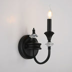 Close view of a black Clérachic wall light with one candle bulb, a round backplate and faceted crystal details on the arm.