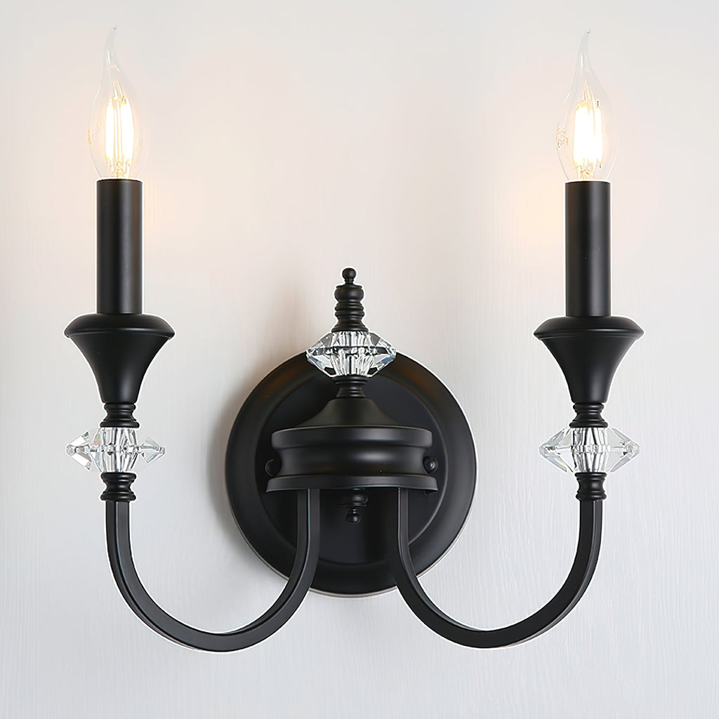 Front view of a black two-arm Clérachic wall light with two candle bulbs lit, mounted on a pale wall with crystal details.