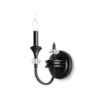Black single-arm Clérachic wall light on a white backdrop, its candle bulb lit above a curved arm and crystal accents.