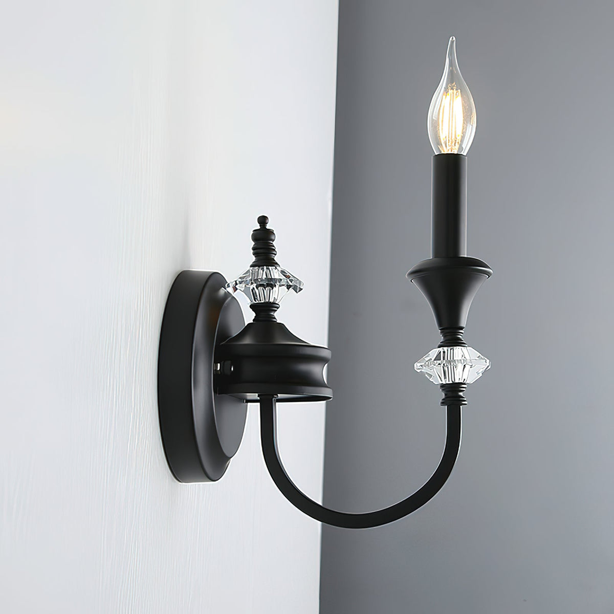 Side view of a black single-arm Clérachic wall light on a grey wall, its curved iron arm reaching out from a round backplate.