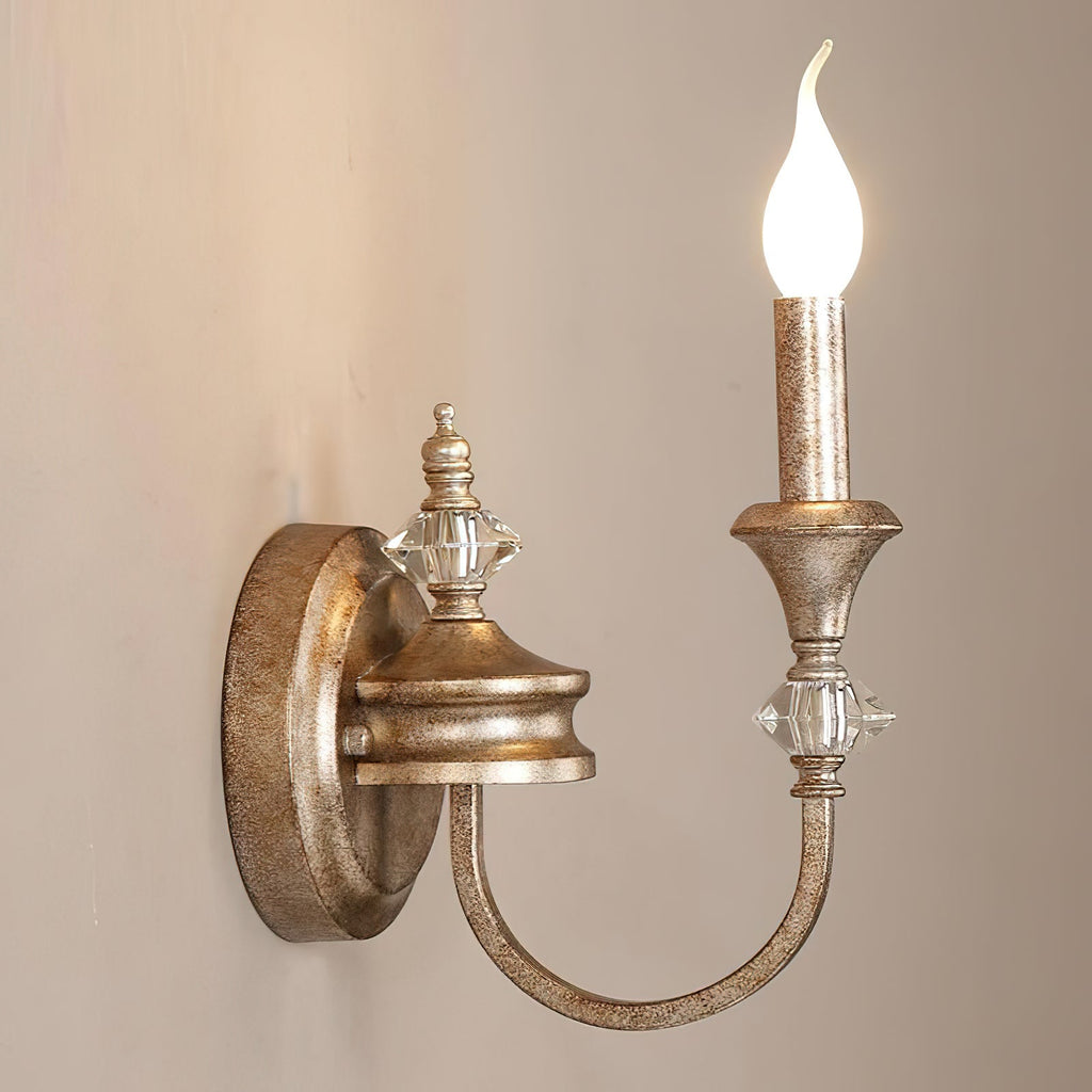 Close side view of a rusty silver single-arm Clérachic wall light, its flame-tip bulb glowing above crystal and metal detailing.