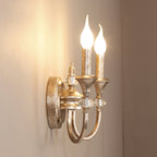 Angled view of a rusty silver two-arm Clérachic wall light with both bulbs lit, casting a warm glow on the wall.