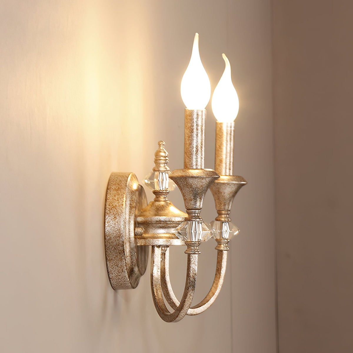 Angled view of a rusty silver two-arm Clérachic wall light with both bulbs lit, casting a warm glow on the wall.
