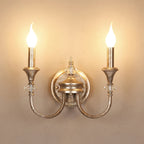 Front view of a rusty silver two-arm Clérachic wall light, both flame-tip bulbs glowing evenly on a warm wall.