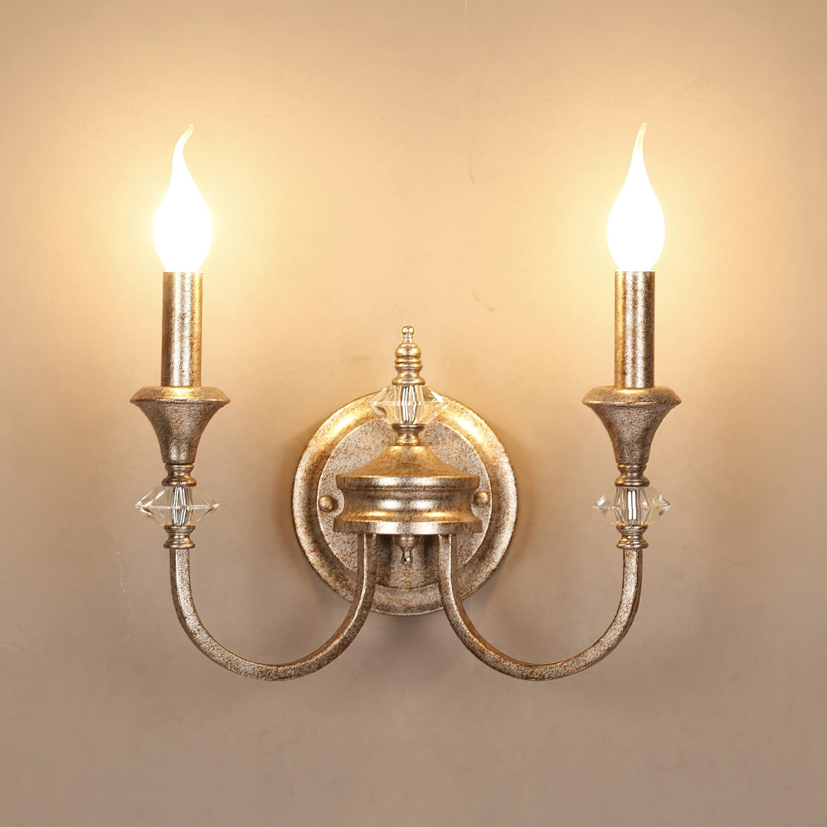 Front view of a rusty silver two-arm Clérachic wall light, both flame-tip bulbs glowing evenly on a warm wall.