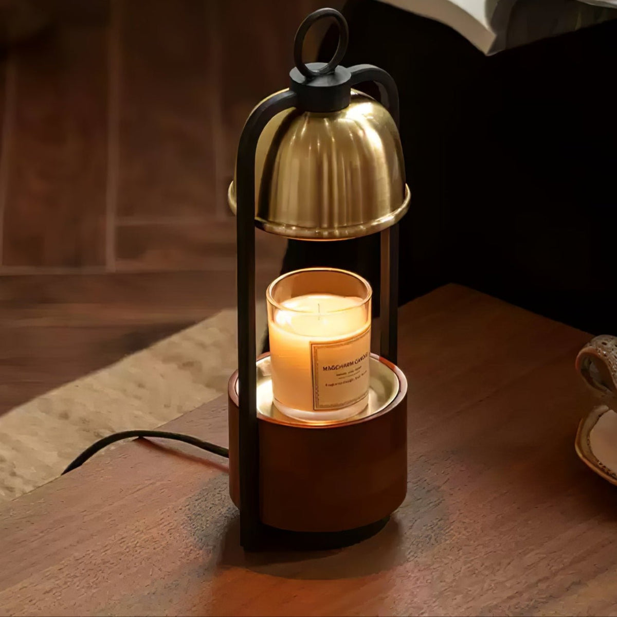 A Clérachic candle warmer lamp on a wooden table, its gold dome above a jar candle that rests on a walnut base, cord trailing behind.