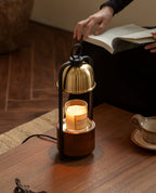Clérachic candle warmer lamp with a gold dome on a wooden side table, as a hand turns the page of an open book above it.