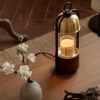 This Clérachic candle warmer lamp stands on a walnut table beside a small vase of white blossom, the candle softly lit beneath its dome.