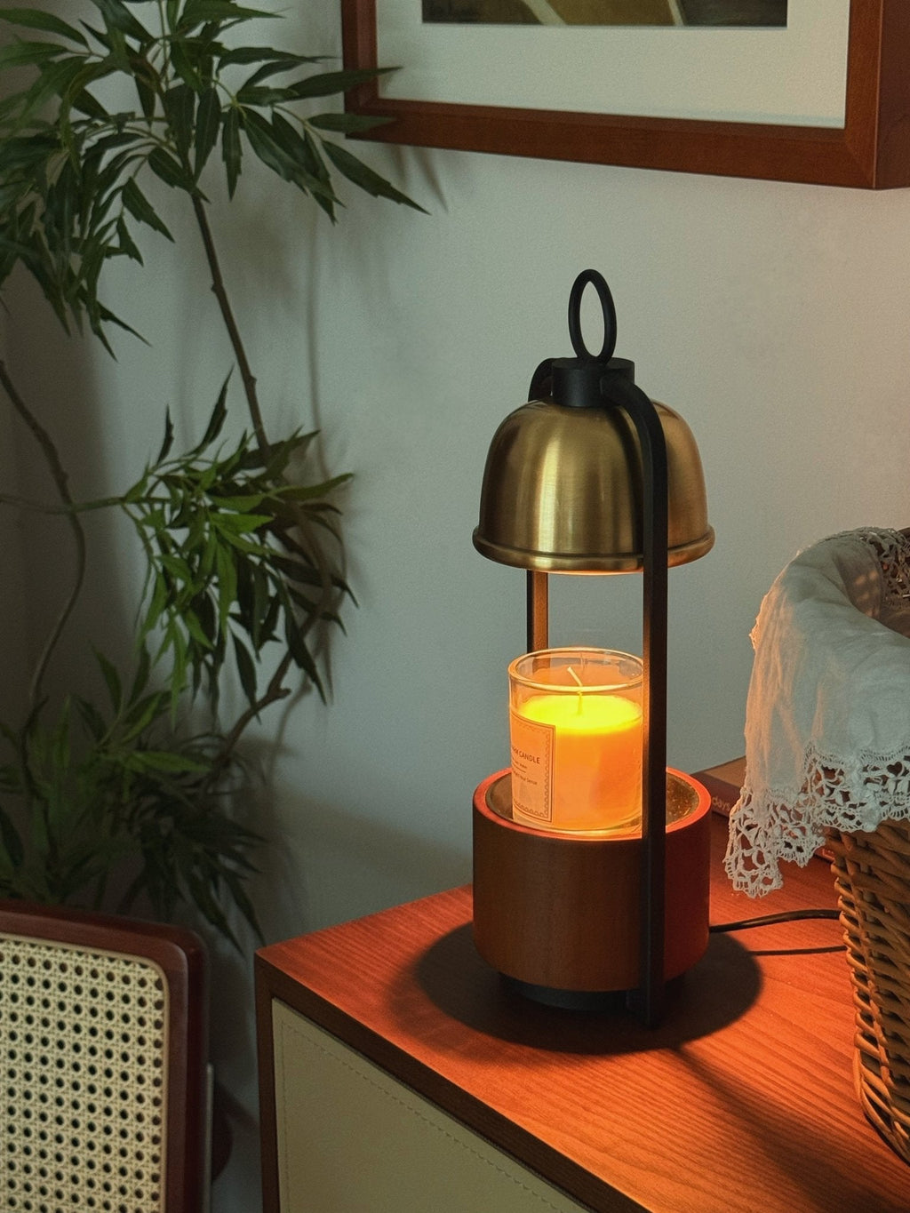 Close-ish view of the Clérachic candle warmer lamp on a chest of drawers, the melted candle glowing orange below the gold dome.
