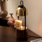 A hand lowers a jar candle onto the warming plate of this Clérachic candle warmer lamp, under its raised gold dome.