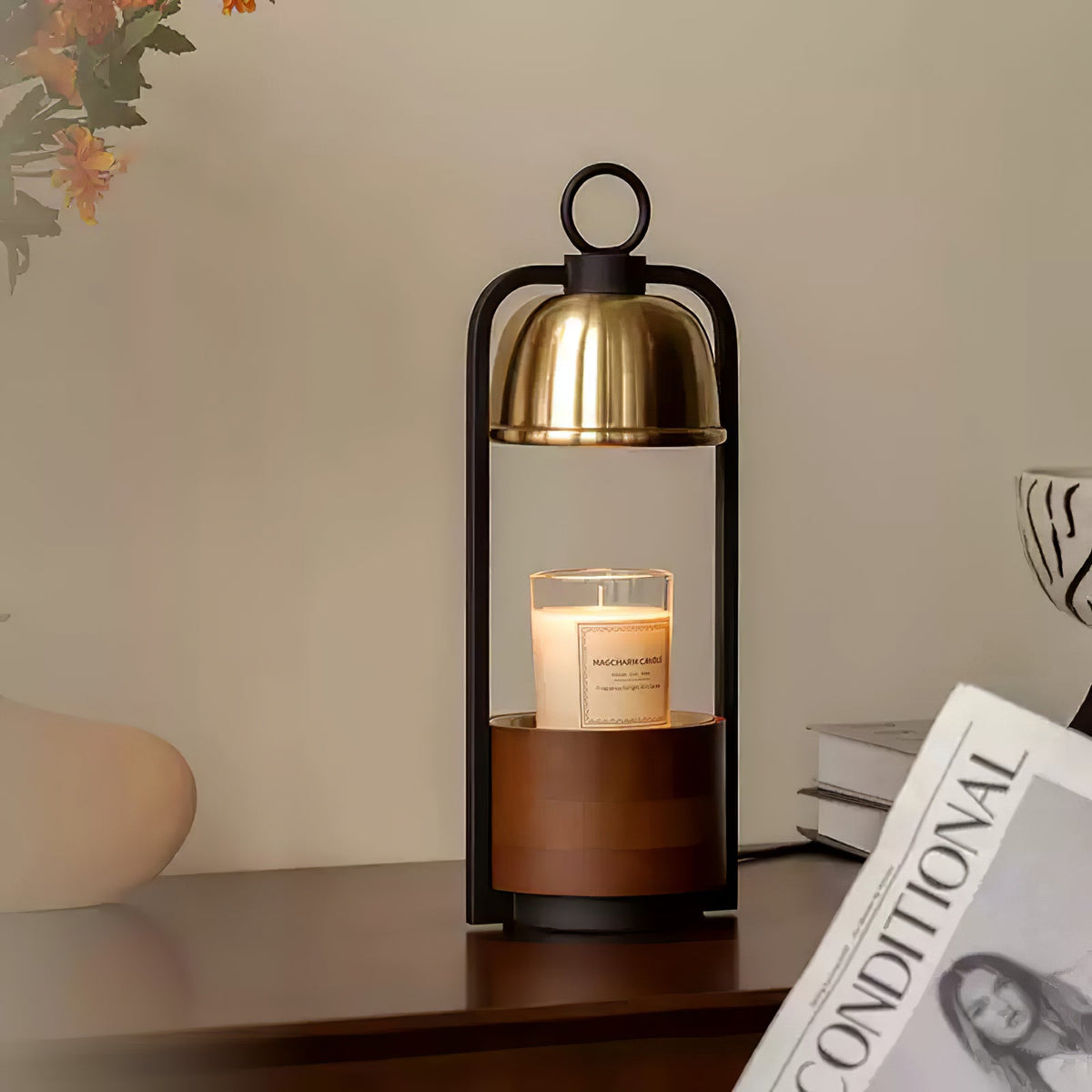 Clérachic candle warmer lamp on a dark wood shelf beside a magazine and a vase, its gold dome over a cream candle.
