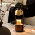 A Clérachic candle warmer lamp lit on a stone-topped table, the candle glowing under the dome, with a person reading behind.
