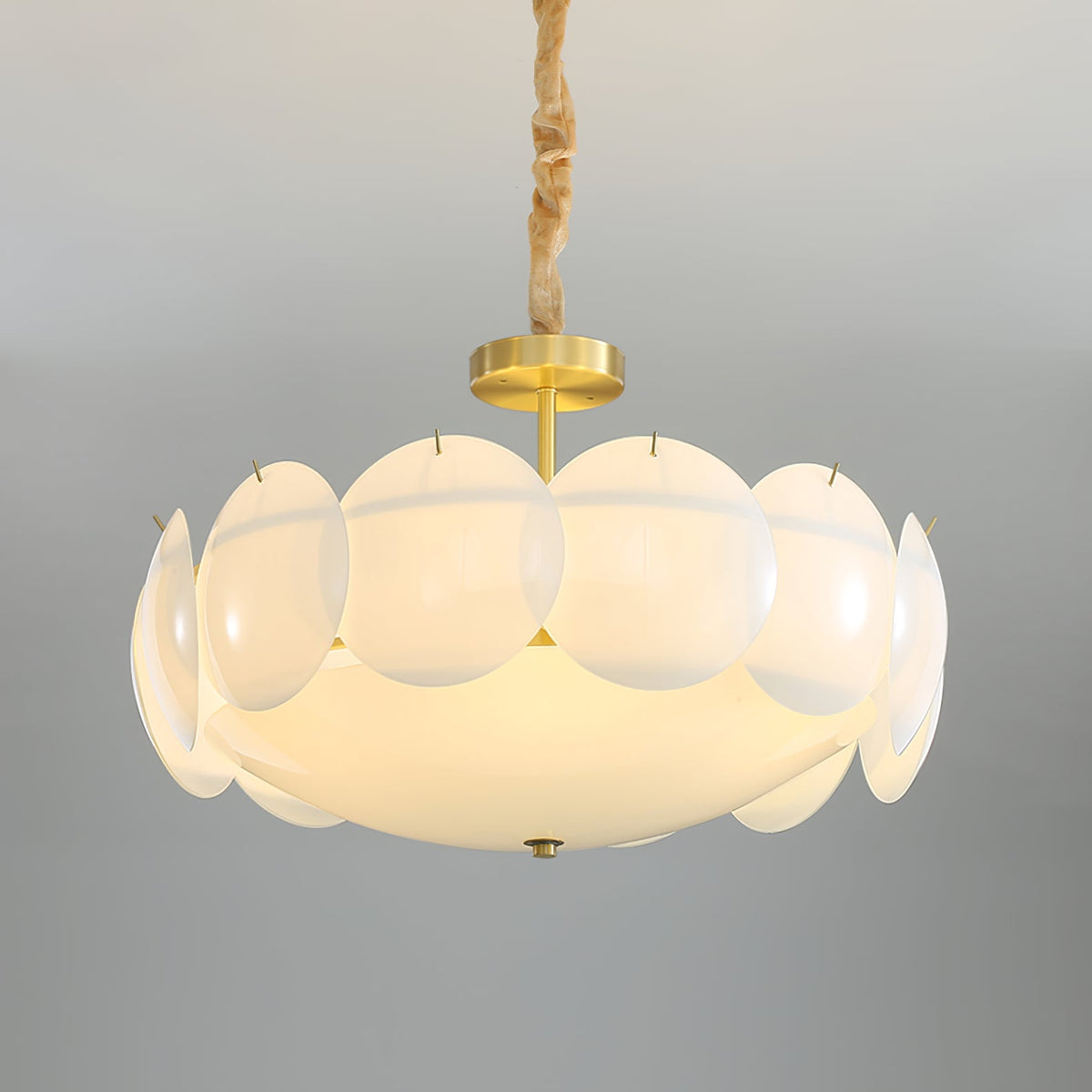 Brass canopy and stem above the ring of round, frosted white shades on this Clérachic chandelier, seen against a soft grey backdrop.