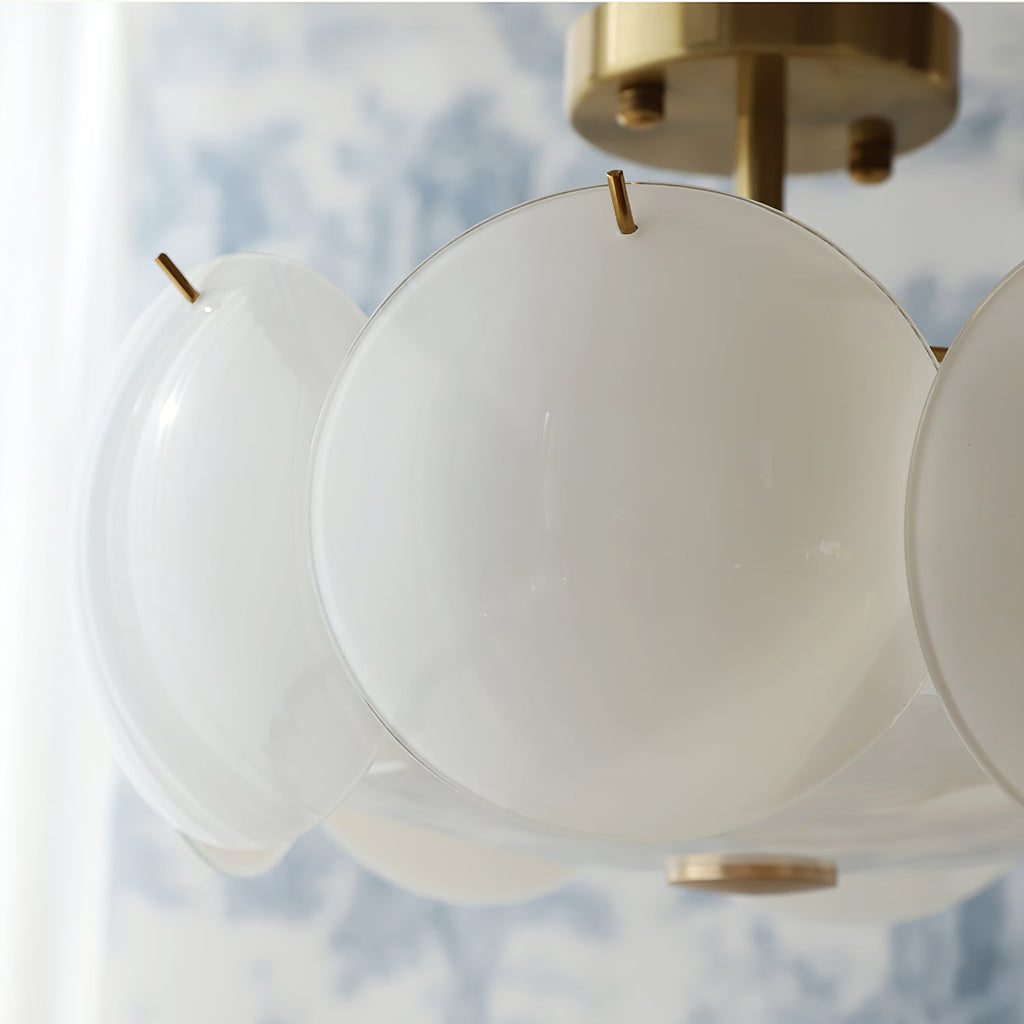 Close view of a single frosted round shade and the brass canopy of this Clérachic chandelier, with blue toile wallpaper behind.