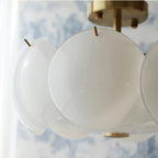 Close view of a single frosted round shade and the brass canopy of this Clérachic chandelier, with blue toile wallpaper behind.