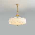 Slightly closer view of this Clérachic chandelier lit, its shell shades and brass details shown against a light grey wall.