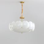 Unlit Clérachic chandelier with frosted white shades on a brass stem and chain, shown against a pale grey backdrop.