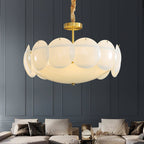 Lit Clérachic chandelier with a warm glow hung in front of a dark blue panelled wall above a cream sofa and cushions.