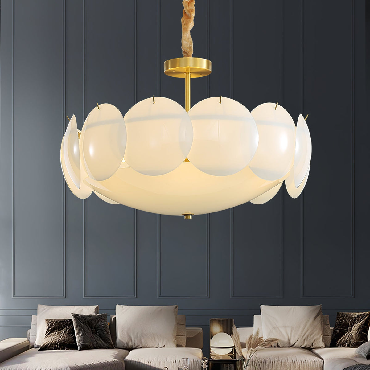 Lit Clérachic chandelier with a warm glow hung in front of a dark blue panelled wall above a cream sofa and cushions.