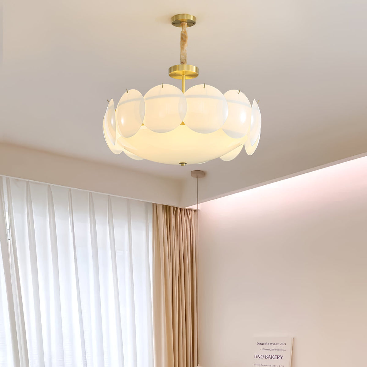 Clérachic chandelier lit and hanging high in a room with white curtains, gold drapes and a pink-washed cove ceiling.