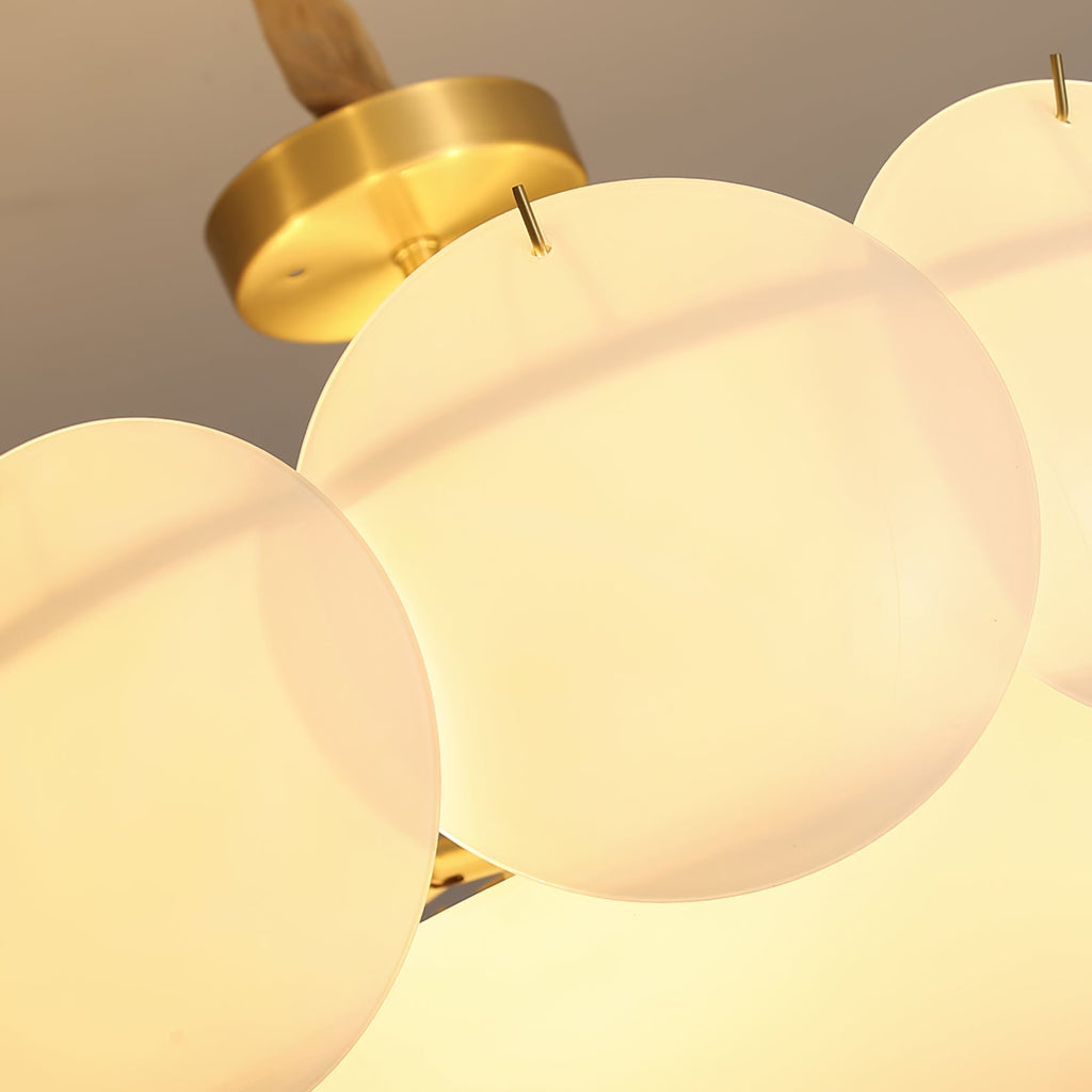 Close view from below of glowing round white shades and a brass canopy on this Clérachic chandelier.