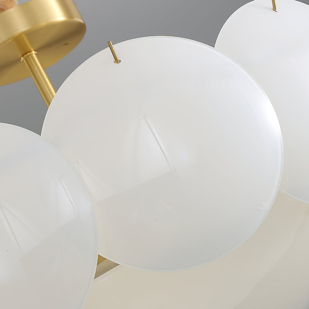 Close view of large, frosted round shades fixed by brass pins on this Clérachic chandelier, with a grey wall behind.