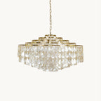 A Clérachic chandelier with tiers of teardrop capiz shell discs on a gold frame, hung from a fine chain on a plain off-white backdrop.
