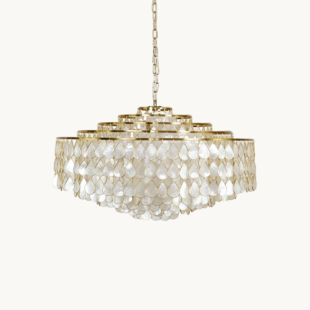A Clérachic chandelier with tiers of teardrop capiz shell discs on a gold frame, hung from a fine chain on a plain off-white backdrop.