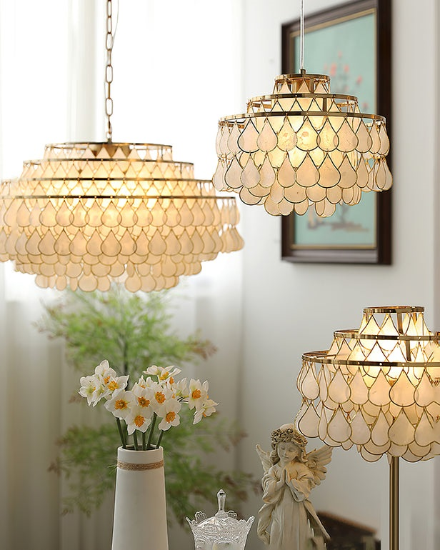 Two Clérachic chandeliers hang above a vase of narcissi and a small angel figure, with a matching floor lamp at the lower right.