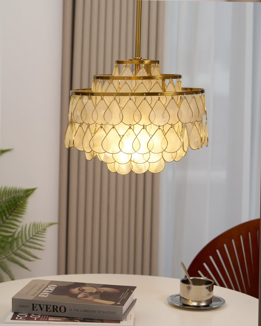 This Clérachic chandelier hangs above a round white table by a ribbed curtain, its gold rings holding warm-lit shell teardrops.