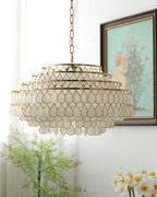 Hung from a fine chain beside a framed painting, this Clérachic chandelier is a wide stack of gold rings and white shell discs.