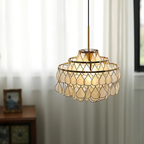 In front of long white curtains and a small framed photo, this Clérachic chandelier glows softly through its shell teardrops.