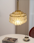 Above a round table with books and a coffee cup, this Clérachic chandelier hangs from a gold rod beside a ribbed curtain.