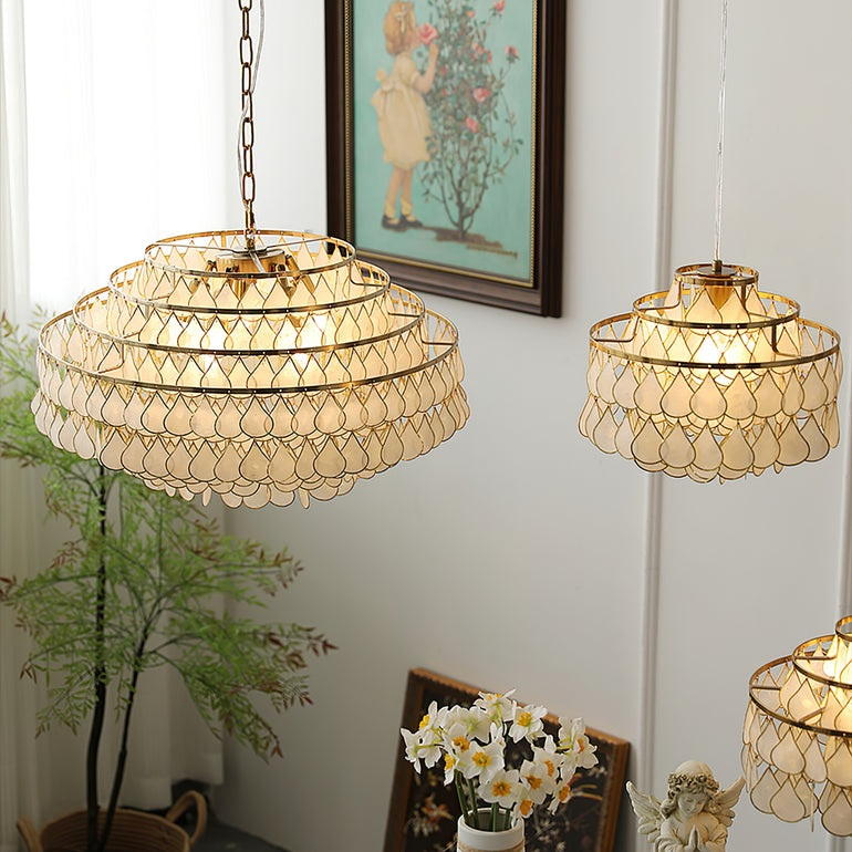 Three Clérachic chandeliers lit warm against a white wall with a framed painting, a pot plant and a small angel figure beneath.