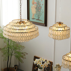Three Clérachic chandeliers lit warm against a white wall with a framed painting, a pot plant and a small angel figure beneath.