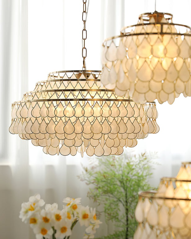Seen close and from below, this Clérachic chandelier on a chain glows warm, with a second shell fitting behind it and white flowers.