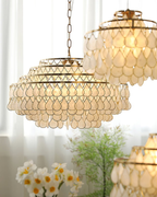 Seen close and from below, this Clérachic chandelier on a chain glows warm, with a second shell fitting behind it and white flowers.