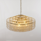 A wide Clérachic chandelier on a short chain, its four gold rings stacked above capiz shell teardrops, shown on a pale grey wall.