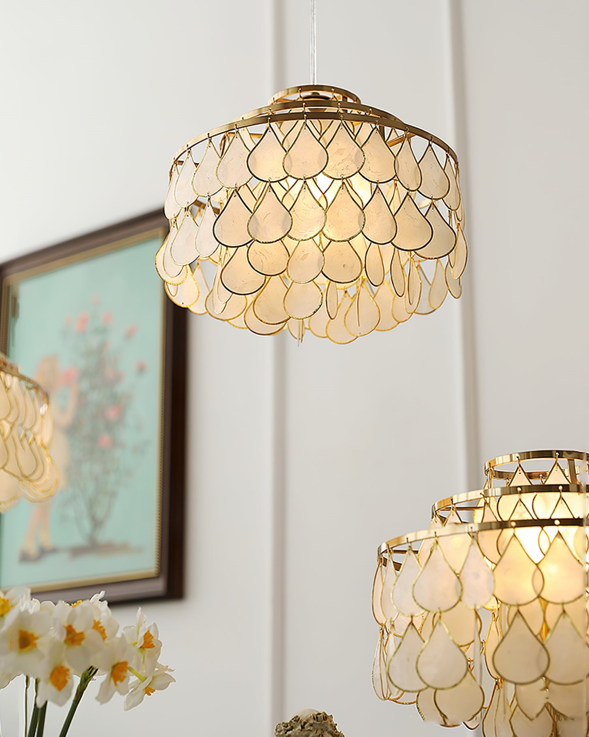 Close to the camera, this Clérachic chandelier glows warm above a framed painting, with other shell fittings and flowers below.
