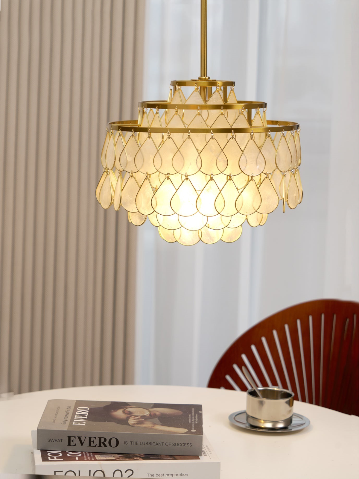 This Clérachic chandelier hangs in front of a ribbed curtain and a round table, its teardrop shells glowing from a bulb inside.