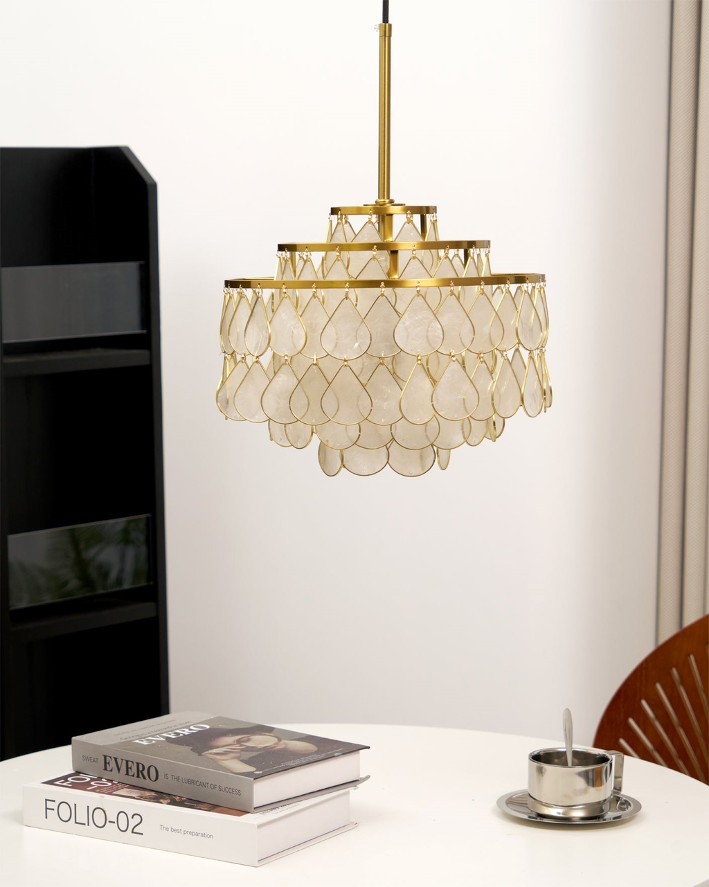 On a gold rod beside a bookcase and a round table, this Clérachic chandelier shows overlapping shell teardrops lit warm from within.