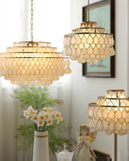Several Clérachic chandeliers near a vase of narcissi, with the closest in the upper left and a floor lamp version at lower right.